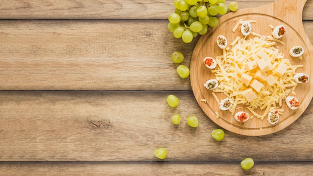Cheese with toppings on chopping board with grapes