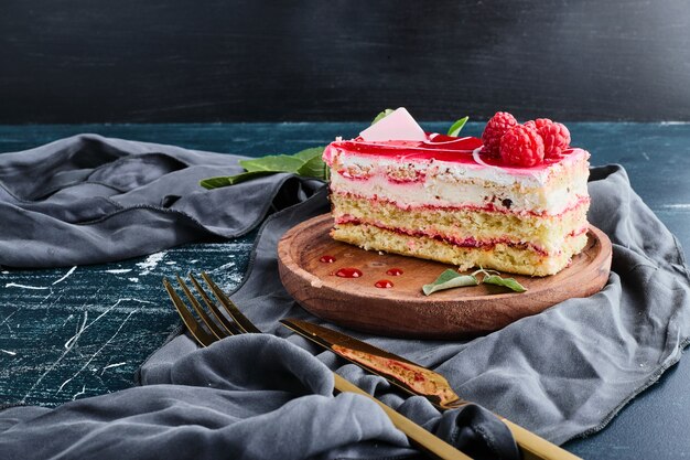 Cheesecake slice with raspberry syrup isolated on blue background on a wooden platter. 