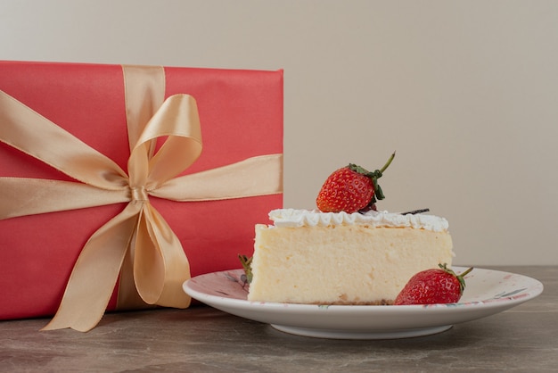 Cheesecake with strawberries and a gift on marble table.