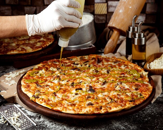 Chef adding pesto sauce to meat pizza