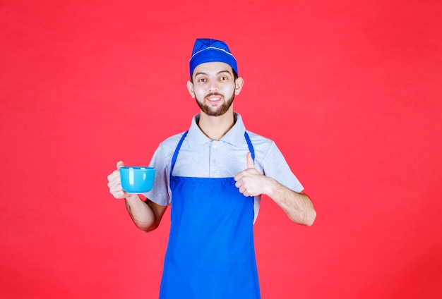 Chef in blue apron holding a blue ceramic cup and enjoying the taste of the product. 