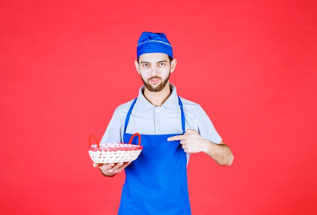 Chef in blue apron holding a bread basket covered with red towel. 