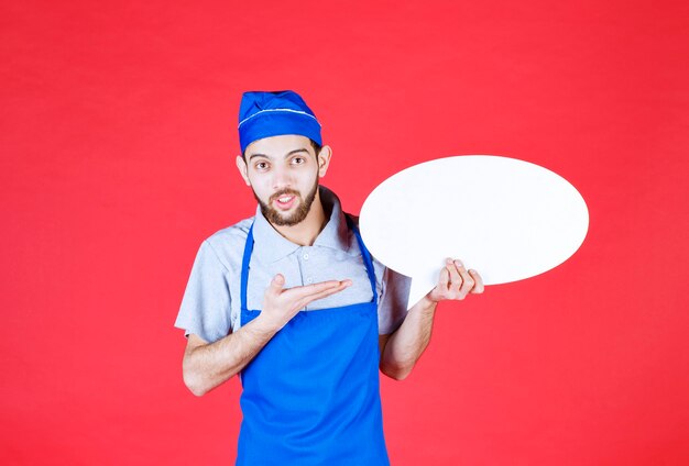 Chef in blue apron holding an ovale info board. 