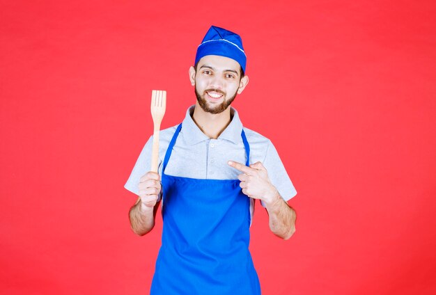 Chef in blue apron holding a wooden spatula. 