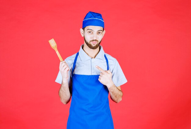 Chef in blue apron holding a wooden spatula. 