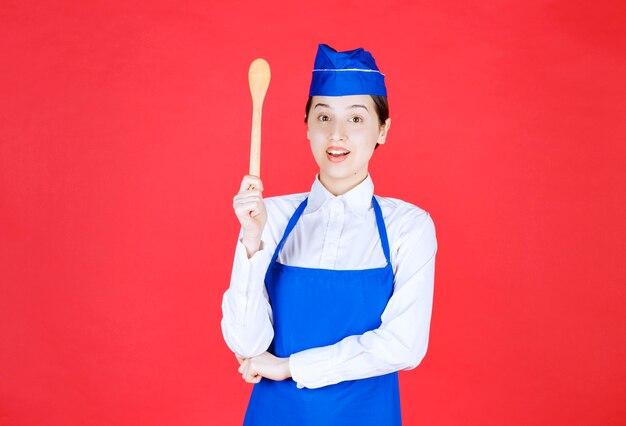 Chef in blue apron holding a wooden spoon. 