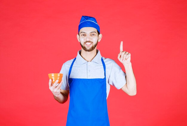 Chef in blue apron holding a yellow ceramic cup and thinking. 