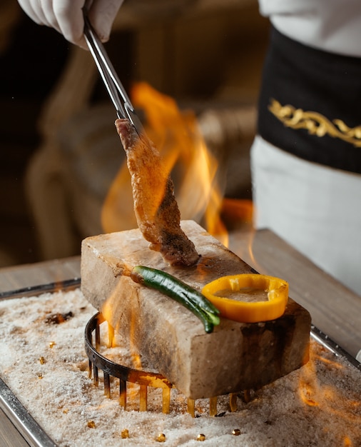 chef cooking beef steak piece with clip on stone brick on fire