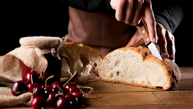 Foto gratuita cuoco unico che taglia il pane con vasetto di marmellata di ciliegie