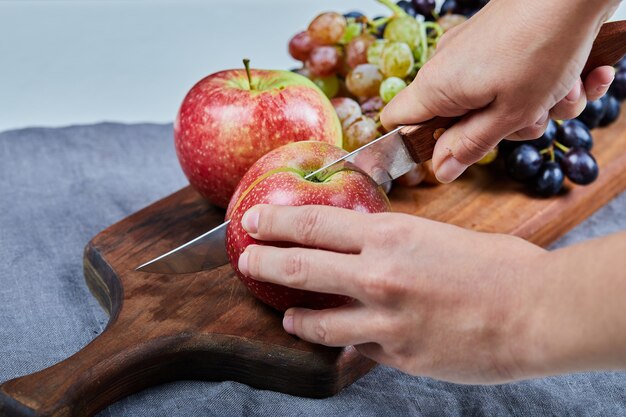 Chef cutting a red apple with a knife on the board. 