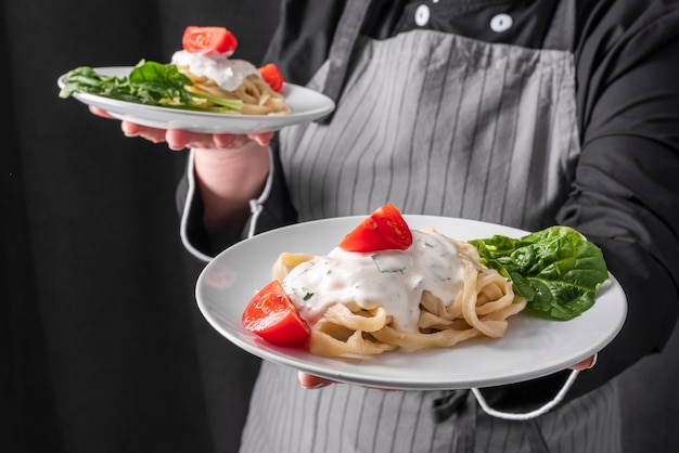 Chef holding pasta dish with sauce and tomatoes