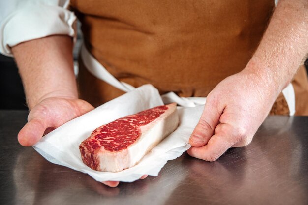 Шеф-повар держит стейк из сырой говядины в пергаментной бумаге Premium Фотографии