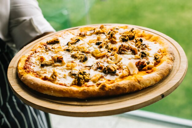 Chef holding seafood pizza with shrimp, mussels, calamari, squid and cheese