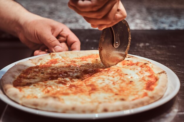 Chef is cutting traditional margarita pizza for customers with special knife.