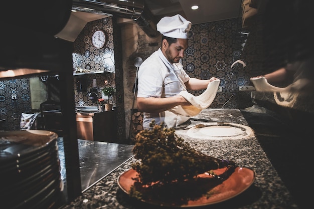 Chef is working on nicely decorated kitchen, preparing pastry for pizza.