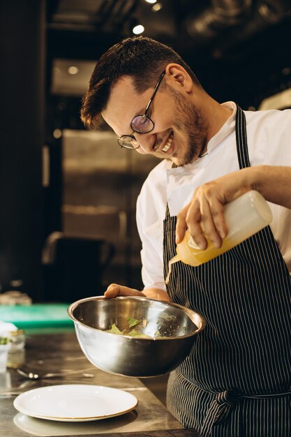 Chef at kitchen in a restaurant adding sauce to the salad