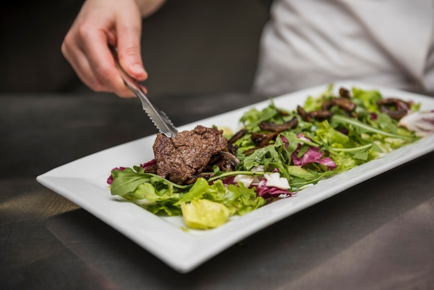 Chef placing beef meat on salad