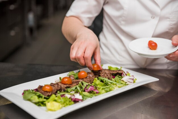 Chef placing fresh tomatoes on salad