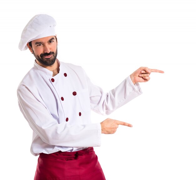 Chef pointing to the lateral over white background