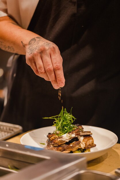 Chef pouring seasoning on beef stake on plate