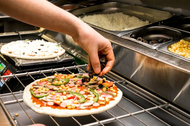 Chef puts olive on pizza dough covered with tomato sauce