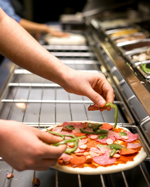 Lo chef mette il pepe sulla pasta della pizza ricoperta di salsa di pomodoro