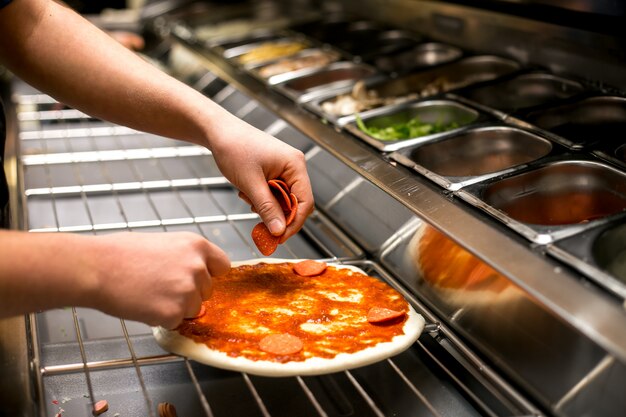 Chef puts pepperoni on pizza dough covered with tomato sauce