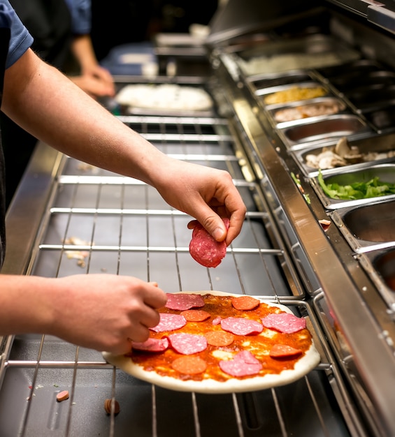 Chef puts sausage on pizza dough covered with tomato sauce