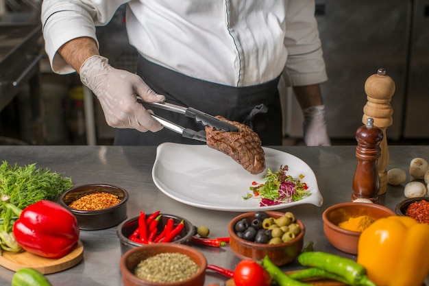 Chef putting grilled steak to the serving plate with herbs salad