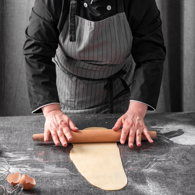 Бесплатное фото Шеф-повар раскатывает тесто на столе