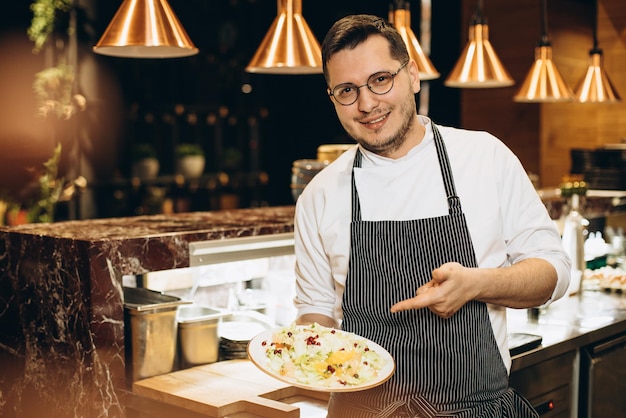 Бесплатное фото Шеф-повар подает салат и стоит у кухонной стойки