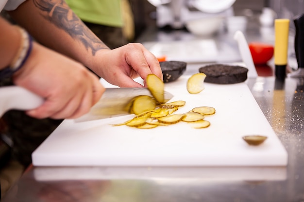 Chef slices pickles for delicious burger in restaurant. Food preparation