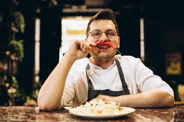 Chef standing by the counter serving salad from cabbage and holding chilli pepper