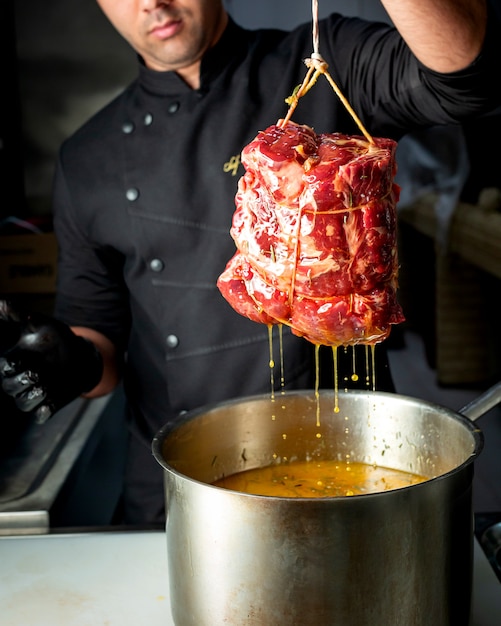 Chef prendendo carne di manzo marinata dalla padella con olio ed erbe