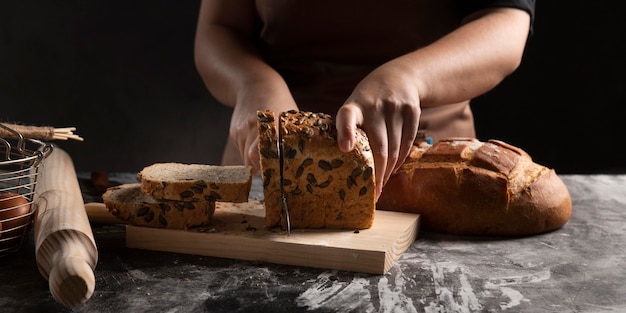 La mano del cuoco con un coltello affetta il pane su un tagliere da cucina