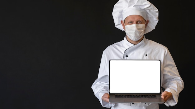 Chef with medical mask holding laptop