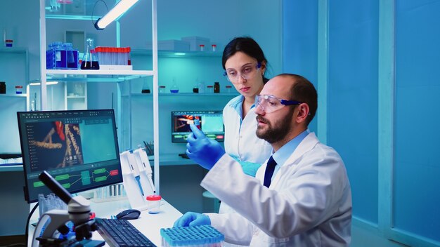 Chemist doctor explaining to nurse vaccine development in modern equipped laboratory holding test tube with blood sample