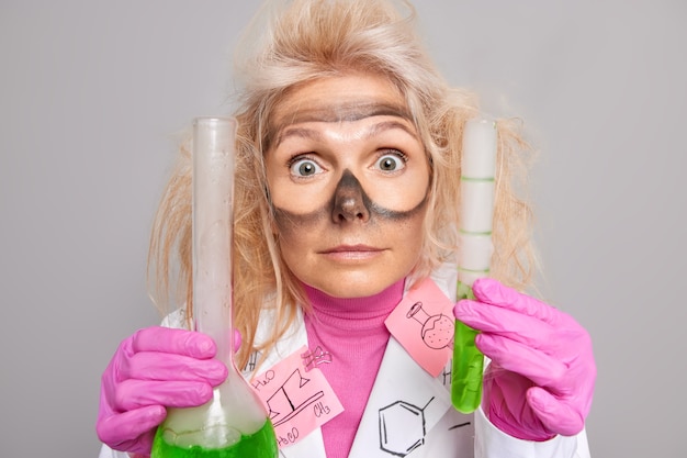化学者の調査員は、保護メガネを着用した後、緑色の液体が目の周りに汚れた痕跡があるガラス製品を持っています。実験実施後の実験室での爆発