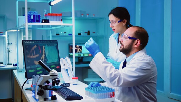 Chemist nurse holding test tubes bringing to doctor conducting DNA experiment discussing about medical treatment working overtime