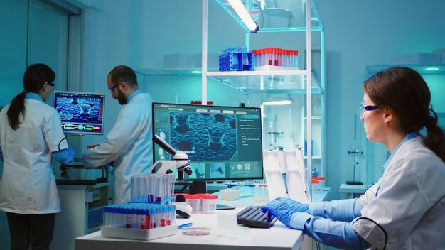Медсестра-химик сидит в лаборатории с научным оборудованием и изучает эволюцию вируса, используя высокотехнологичное лечение против вируса covid19