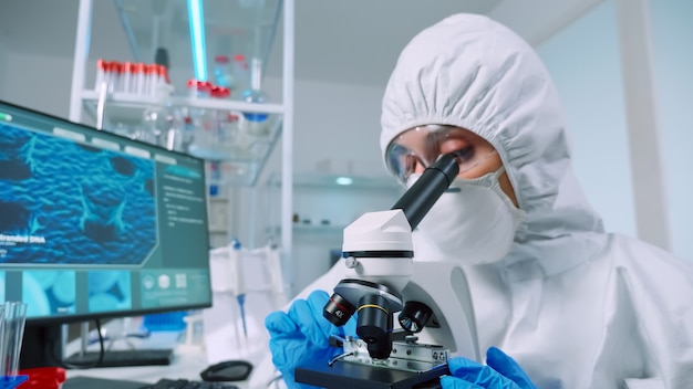 Chemist researcher wearing coverall in sterile lab doing experiments for medical industry using microscope. Doctors examining virus evolution using high tech for vaccine development against covid19