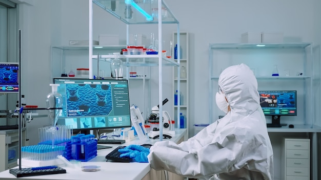 화학자는 PC에 타이핑을 하고 동료는 장비를 갖춘 실험실에서 현미경 슬라이드를 분석합니다. covid19 바이러스에 대한 치료법을 연구하기 위해 첨단 기술을 사용하여 백신 진화를 조사하는 과학자 팀