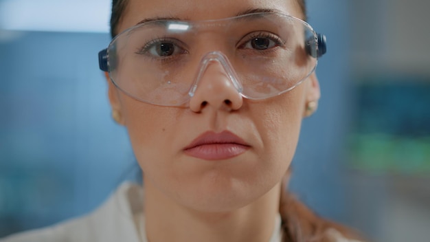 Chemist woman looking at camera in science laboratory, wearing eyeglasses for safety and protection. Portrait of biology researcher with protective goggles working in lab. Close up