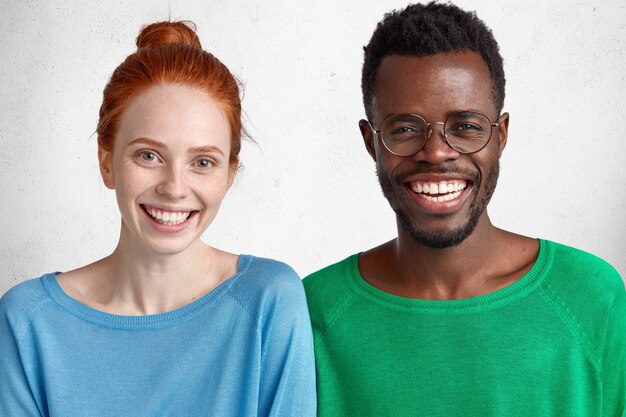 Cherful freckled ginger woman and male stand closely, show white teeth, rejoice meeting, isolated over concrete studio wall