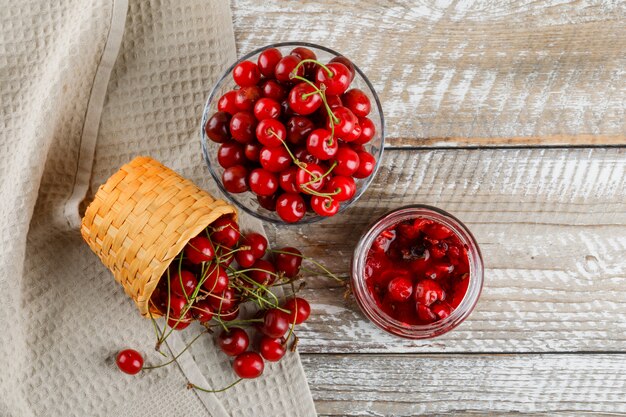 Cherries in bowl and basket with jam on wooden and kitchen towel