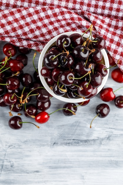 Free photo cherries in a bowl on grungy and picnic cloth surface. flat lay.