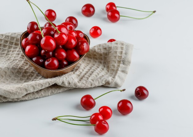 Cherries in a bowl high angle view on white and kitchen towel