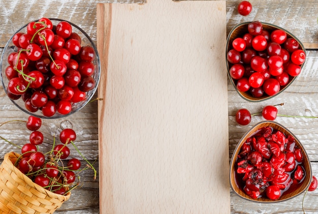 Cherries in bowls and basket with jam on wooden and cutting board