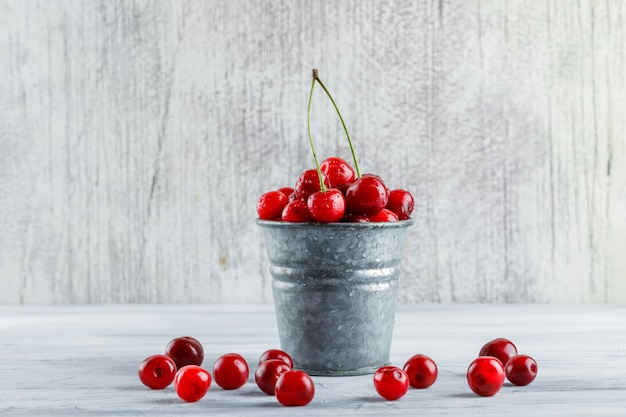 Cherries in a mini bucket on a grungy grey. side view.