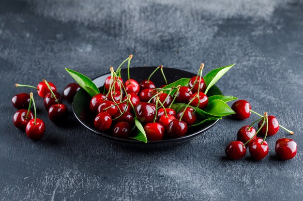 Cherries in a plate with leaves high angle view on a grey plaster surface